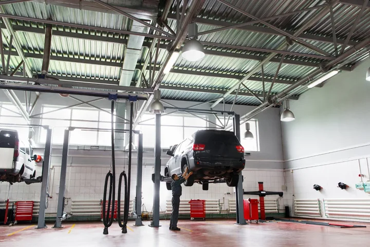 Mechanik sprawdzający podwozie uniesionego SUV-a w jasnym warsztacie samochodowym z podnośnikami