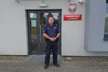 Funkcjonariusz policji w mundurze stoi przed wejściem do Komisariatu Policji w Łodygowicach.